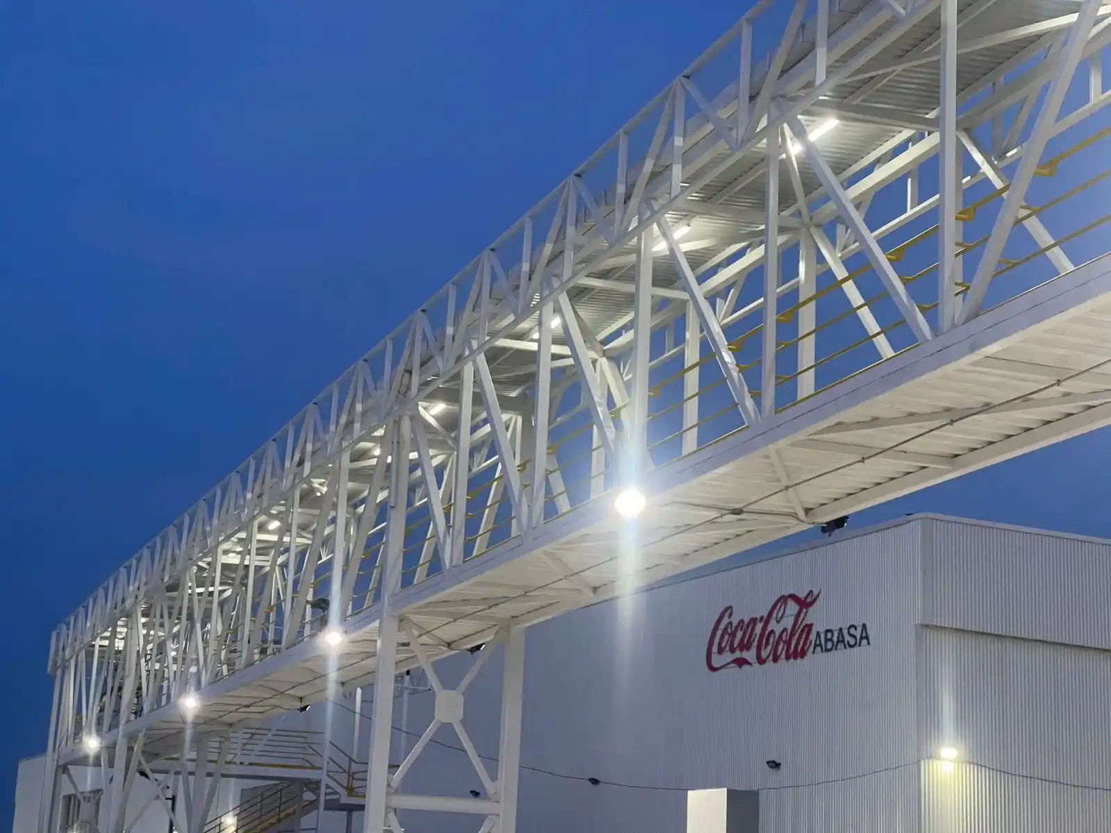Pasarela industrial elevada con sistema de iluminación exterior en planta de Coca-Cola